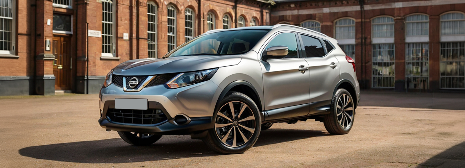 A Nissan Qashqai, a compact crossover SUV parked in front of an old brick building